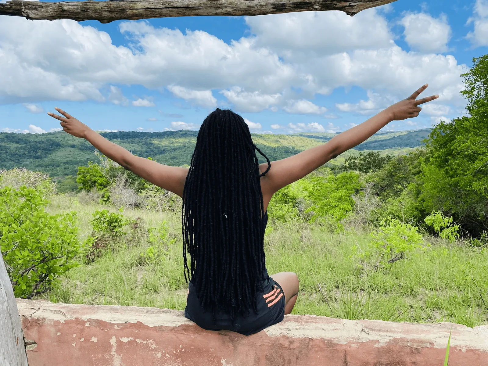 A-young-woman-with-long-black-hair-_dreadlocks_-and-arms-stretches-sitting-on-a-concrete-wall-overlooking Shimba Hills