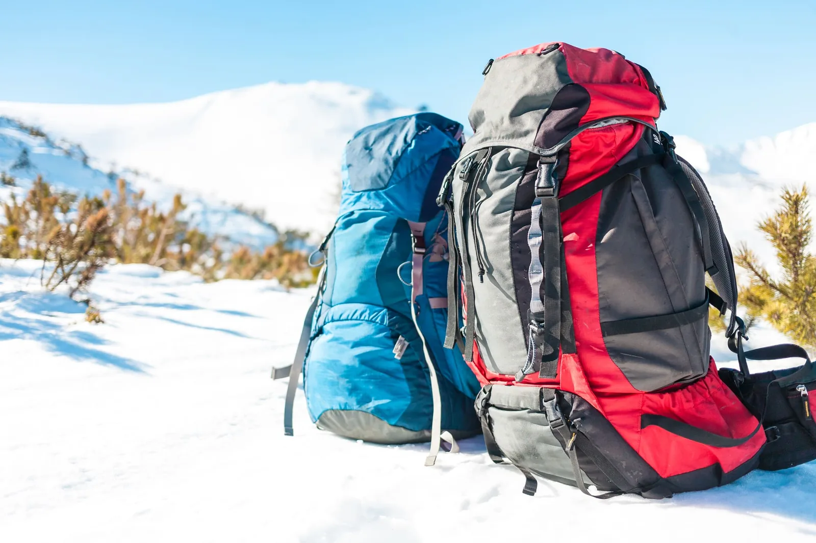 Two backpacks in the background of snow-capped mountains and blue sky. A backpack on the snow. Active lifestyle. Trekking in winter.